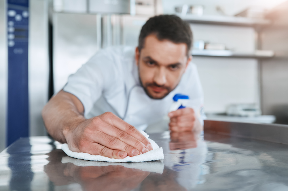 Bearded man prepares the surface for cooking in the kitchen. He carefully wipes the surface using a spray for it. Health and safety concept. Close up